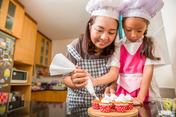 Asian mother and daughter enjoy making and decorate bakery cake in real life kitchen, Concept of family cooking