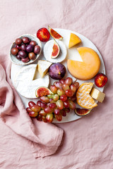 Appetizers, antipasti snacks. Cheese and fruit platter on marble board over pink linen tablecloth background. Top view