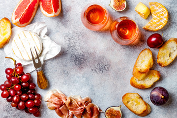 Appetizers, antipasti snacks and rose wine in glasses. Cheese and meat platter over grey concrete background. Frame, copy space, top view