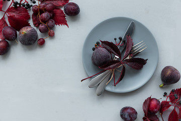 Table settings, purple girlish (wild) grape leaves, grapes, plums and figs on gray wooden background. Top view. Flat lay. Autumn harvesting or Thanksgiving celebration concept.