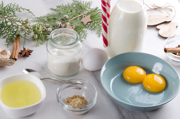Closeup of fresh ingredients for eggnog.Concept of process of making traditional Christmas drink.Bottle of milk, jar of sugar, broken eggs, decorations on the white table