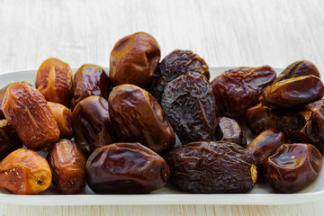 Dates of different grades lie on a white rectangular dish on a white wooden background