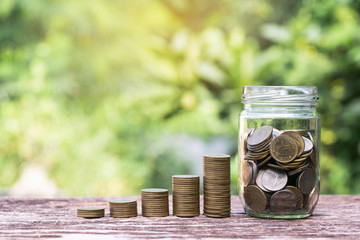 Coins in glass jar  Set on wooden plate, put in a green park background also some coins beside.