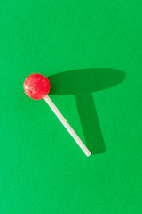 Red lollipop on a bright green background. The concept of sweets, junk food. Copyspace.