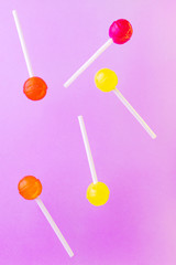 Red, orange and yellow lollipops on a lilac background. Zero gravity banner. Levitation. Copyspace. The concept of sweets, junk food.