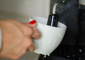 Woman's hand preparing fresh capuccino or coffee on a coffeemaker. barista making coffee using a modern coffee machine. streaming milk for make cappuccino. Close up