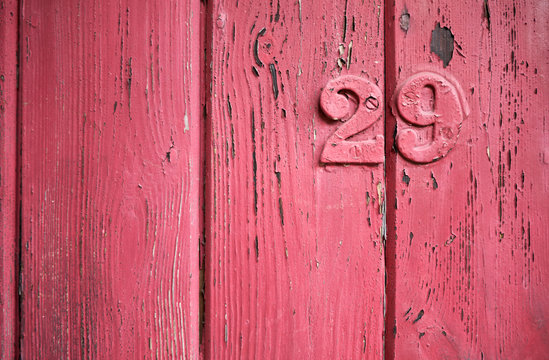 Rustic aged closeup of wood panel painted with red chipping colour. Vertical slats with vertical wood lines texture and metal number 29 over painted