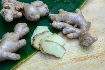Fresh ginger root and ginger sliced on green leaf background on wood table background, healthy Asian herb concept