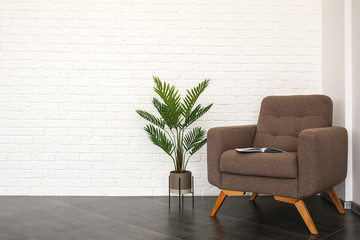 Stylish armchair with tropical plant near white brick wall in room