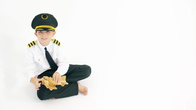 Boy wearing pilot's uniform plays with generic wooden toy plane on white background
