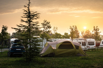 Caravans and tent on green meadow in campsite. Sunrise, rays on campers and tent in the morning....