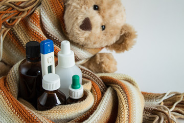 A Teddy bear wrapped in a warm scarf and bottles of medicine and a thermometer
