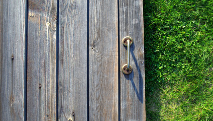 Doorknob on the background of old dark boards with soft green grass