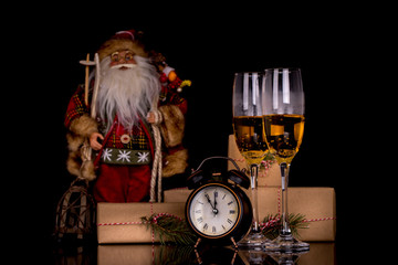 Two wine glasses with champagne, Santa Claus, clock and christmas gifts on a black background