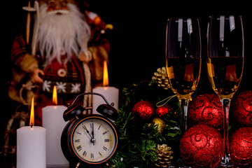 Two wine glasses with champagne, Santa Claus, clock and christmas ornaments on a black background
