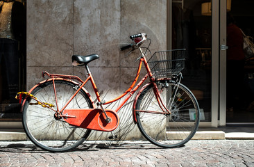 Fototapeta na wymiar Red bike with basket on italian street. Typical italian architecture on background.