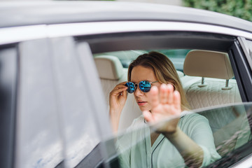 Naklejka premium Young woman with sunglasses sitting on back seat of car, hiding from paparazzi.