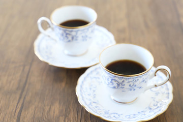 木製テーブルの上に乗った白い陶器のカップ&ソーサーにブラックコーヒー