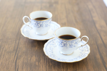 木製テーブルの上に乗った白い陶器のカップ&ソーサーにブラックコーヒー