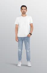 Standing male model wearing white plain crew neck t shirt in ripped blue denim jeans pant. Isolated...