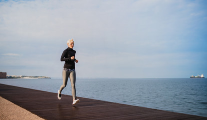 Side view of young sportswoman running outdoors on beach.