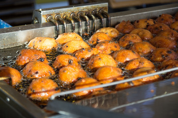 Close up of oliebollen with currants that are baking in a professional frying pan.
