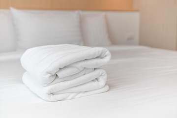 Close-up: The white towels are neatly folded and placed on the white bed. Hotel