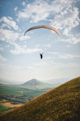 A white-orange paraglider flies over the mountainous terrain