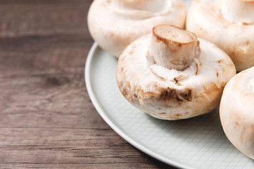 Close-up of white mushrooms on a white plate on a dark wooden table. Vegetarian healthy food