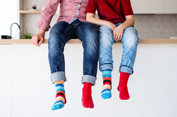 Midsection of father with son with funky socks sitting on kitchen counter indoors.