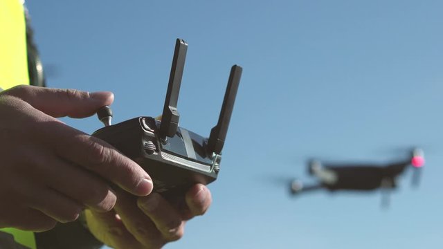 Man drone operator controls an aircraft remote control on a sunny day. Engineer in helmet and vest at a construction site at the construction of the road. Hands with remote control close up