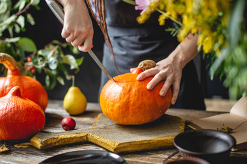 Woman chef cleans an orange pumpkin to prepare for baking. Autumn food in a cozy dark wooden...