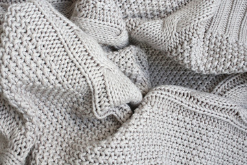 Crumpled beige knitted blanket or plaid. The knitted fabric was soft and warm, wrinkled. Texture for background.