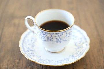 木製テーブルの上に乗った白い陶器のカップ&ソーサーにブラックコーヒー