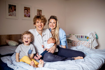 Young parents with newborn baby and small toddler son at home.