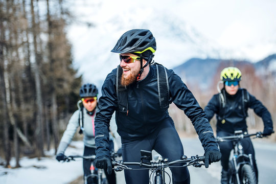 Front view of group of mountain bikers riding on road outdoors in winter.