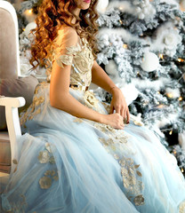 luxurious girl in a beautiful dress sitting beside a Christmas tree with lights