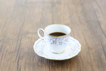 木製テーブルの上に乗った白い陶器のカップ&ソーサーにブラックコーヒー