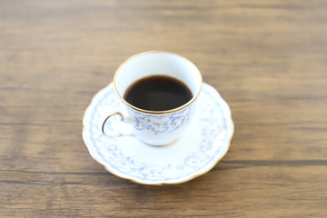 木製テーブルの上に乗った白い陶器のカップ&ソーサーにブラックコーヒー