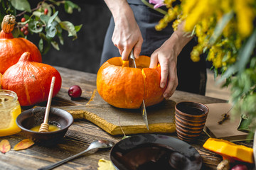 Woman chef cooking an orange pumpkin for baking with honey and cinnamon. Concept autumn food in a dark wooden kitchen