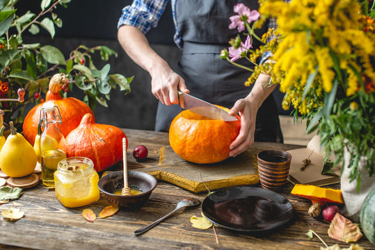 Woman Chef Cooking An Orange Pumpkin For Baking With Honey And Cinnamon. Concept Autumn Food In A Dark Wooden Kitchen