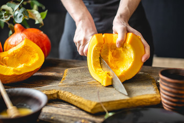 Woman cook cuts an orange pumpkin with a knife into slices for baking. Autumn food in a cozy dark kitchen. Close up