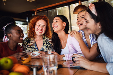 Group of young female friends having fun in cafe, talking and laughing while sitting at table.	