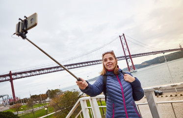 Obraz na płótnie Canvas Young woman tourist take selfies on the background of famous iron 25th of April bridge in Lisbon city, Portugal