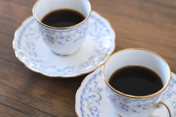 木製テーブルの上に乗った白い陶器のカップ&ソーサーにブラックコーヒー