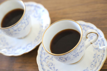 木製テーブルの上に乗った白い陶器のカップ&ソーサーにブラックコーヒー