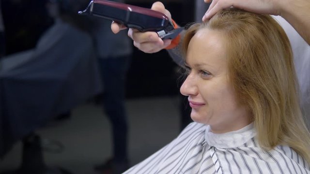 Woman shaving her head baldly. a hairdresser shaves a woman's long hair with a hair clipper.