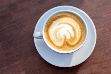 Cup with cappuccino on a wooden table with copy space, an Italian espresso-based hot coffee drink, high angle view from above