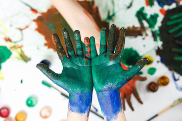 green hands in paints on background of light table painted in different colors
