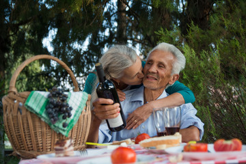 Happy senior woman hugging and kissing her husband on a picnic